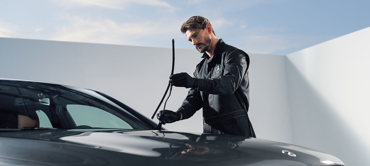 Ein Mitarbeiter prüft die montierten Mercedes-Benz Wischerblätter. Von dem Fahrzeug ist die Frontscheibe und ein Teil der Motorhaube zu erkennen, der Hintergrund ist hell.
