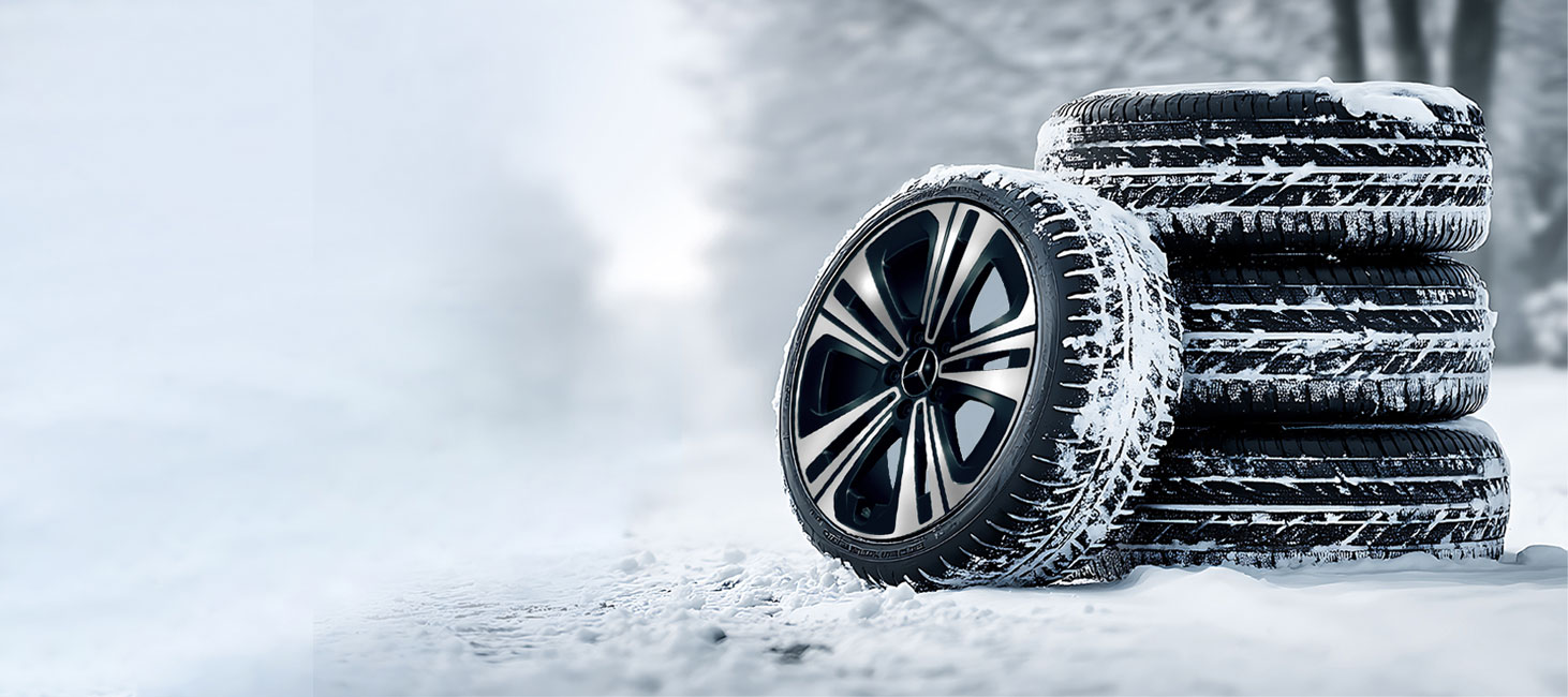 Abgebildet wird ein Radsatz Winterkompletträder von Mercedes-Benz. Ein Rad wurde neben den Stapel gestellt, zur Felgendarstellung. Die Räder stehen auf einer beschneiten Straße.